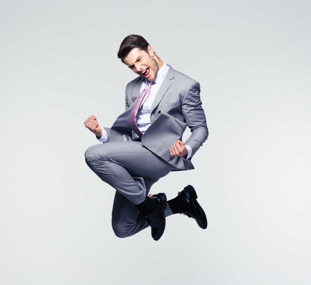 Funny cheerful businessman jumping in air over gray background